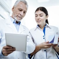Handsome bearded man in a white coat showing a picture on a tablet Report. Handsome bearded man wearing a white coat showing a picture on a tablet to his colleague